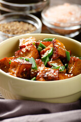 Close Up view at crispy fried tofu pieces with chives and sesame in clay dish