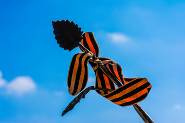 Forged iron leaf wrapped St. George ribbon on a background of blue sky, the celebration of the...