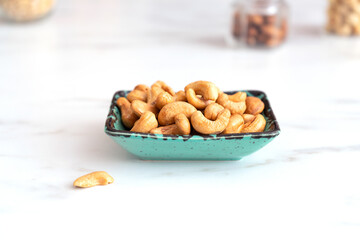 Peeled roasted cashews in a green rectangular plate stands on a white table. Healthy food, tasty and healthy snacks. Foods are high in antioxidants, protein, minerals and vitamins.