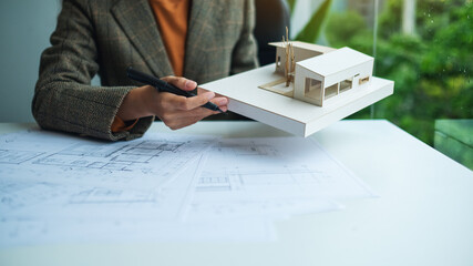 A female architect holding and working on an architecture house model with shop drawing paper in...