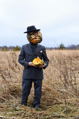 man in a fancy dress celebrates Halloween and and shows a cut up ripe pumpkin standing in an autumn field among dry grasses