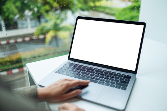 Mockup image of a hand using and touching on laptop computer touchpad with blank white desktop screen