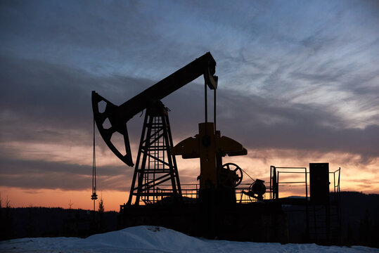 View of evening dramatic sky over long stroke balanced beam petroleum pump jack. Oil field with oil pumping unit or oil pump rocker-machine during sunset. Concept of petroleum industry, oil extraction