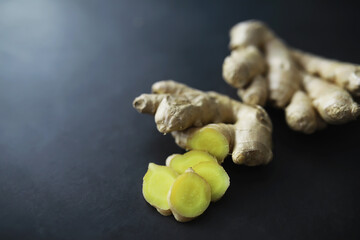 Ginger root whole and sliced. Ginger tea with lemon on the dark background. Fresh ginger root on stone background. Vitamins. Free space for your text.