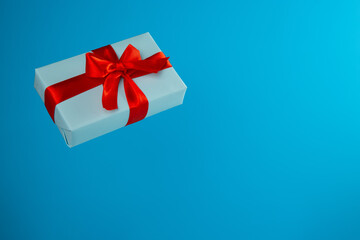 gift box flying in the air is tied with a silk red ribbon on a blue pastel background. The gift is a festive choice.