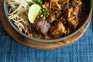 Khanom Jeen Nam ngiao (Spicy Rice Noodle Soup) with spicy pork sauce on dark blue table cloth, Traditional northern Thai cuisine. overhead view