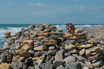 Boy playing, hiding behind a fortress of stones on the beach