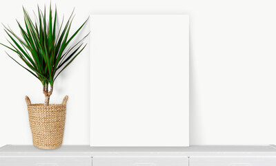 Interior vertical rectangular poster mockup standing on the table with plant and decorations on empty white wall background. Rendering illustration.