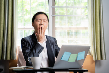 Asian woman working with laptop sitting on the bed at home bored and yawning. WFH. Work from home.