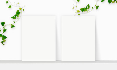 Two Interior vertical rectangular poster mockup standing on the table with plant and decorations on empty white wall background. Rendering illustration.