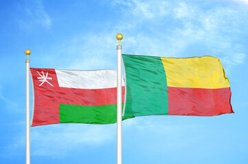Oman and Benin two flags on flagpoles and blue sky
