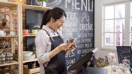 female businesswoman owner of cafe bar counting finances using calculator in small coffeehouse. smiling girl coffeehouse staff joyful with earning money in counter. waitress doing close shop routine