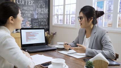 Two female business colleagues having chat gesturing towards laptop computer. beautiful lady coworkers discussing new project with notebook pc in cafe store meeting. elegant women workers talking.