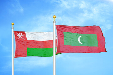 Oman and Maldives two flags on flagpoles and blue sky
