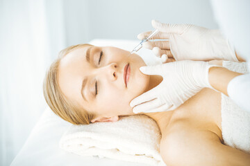 Beautician doctor doing beauty procedure with syringe to blonde female face. Cosmetic medicine, beauty injections concept
