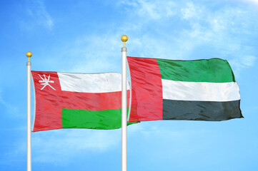 Oman and United Arab Emirates two flags on flagpoles and blue sky