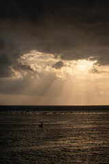 The sun's rays over the sea, burst out of the cloud. Dramatic sunset on the sea, beautiful peaceful scene, rays of light shine in water, sunbeam in cloudy sky, summer ocean view, with fisherman