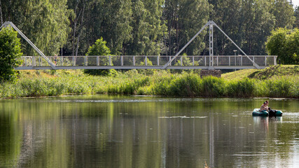 White footbridge over the river in the park. Walk outdoors. Metal bridge. Bridge for pedestrians. People walk across the bridge. Graphic elements of the bridge structure.