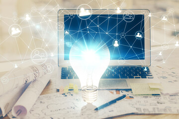 Computer on desktop in office with bulb icon hologram. Multi exposure. Concept of idea.