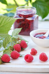 Raspberries and glass jar of jam on white cutting board