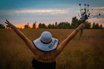 Naklejka na ściany i meble Woman with holiday hat standing in a meadow during sunset