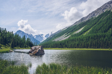 Meditative view to beautiful lake with stone in valley on snowy mountains background. Scenic...