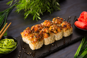 Set of baked sushi rolls with wasabi and ginger on black background. Japanese oriental cuisine