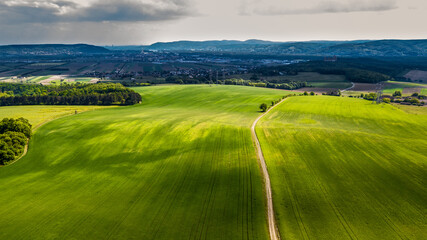 Obraz premium Narrow Gravel Path Between Green Fields in Rural Landscape To City In The Distance In Austria