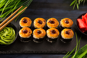 Set of baked sushi rolls with wasabi and ginger on black background. Japanese oriental cuisine