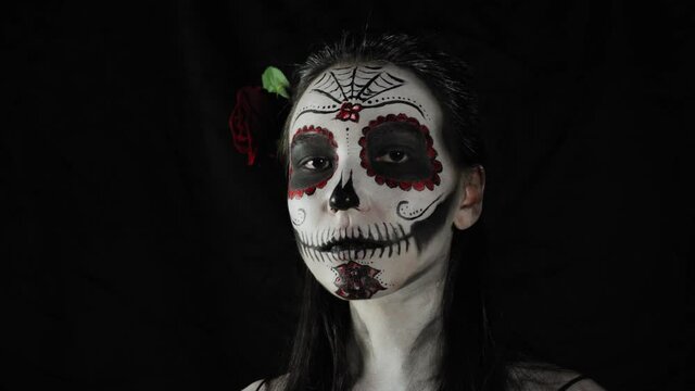Mexican day of the dead. Young woman with sugar skull Halloween makeup looks at the camera. The woman removes the mask from her face. Happy Halloween. High quality 4k video