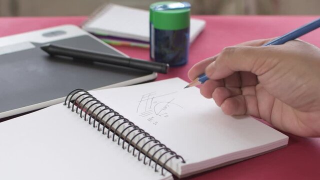 Woman's hands taking notes with a pencil in a notebook, next with a pencil sharpener and graphic tablet in the background.