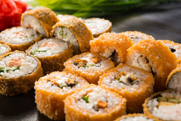 Set of fried sushi rolls with wasabi and ginger on black background. Japanese oriental cuisine