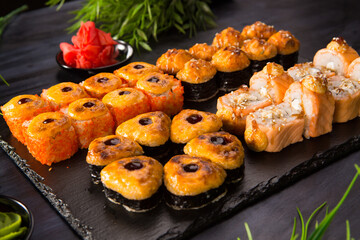 Set of baked sushi rolls with wasabi and ginger on black background. Japanese oriental cuisine