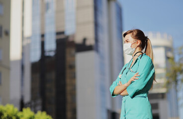 Fototapeta premium Female doctor, nurse wearing a protective face mask in the city. Skyscraper, sky