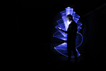 Silhouette of a man using a smartphone. Abstract shape at lightpainting with a light saber. Face illuminated by screen.	