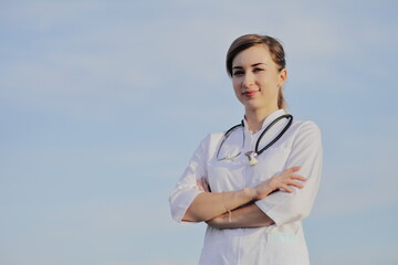 Portrait of a beautiful female doctor or nurse against blue sky with clouds