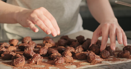 young woman rolling chocolate truffles in cocoa powder on home kictchen