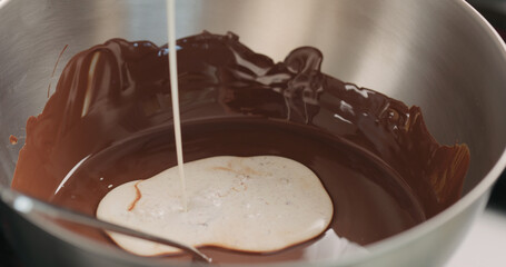 adding cream into melted chocolate in steel bowl