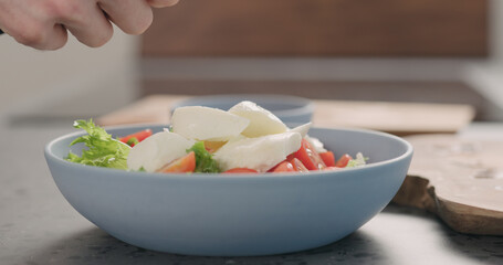 making salad with frisee lettuce, tomatoes amd mozzarella in a blue bowl on kitchen countertop