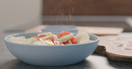 making salad with frisee lettuce, tomatoes amd mozzarella in a blue bowl on kitchen countertop