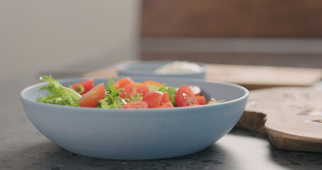 making salad with frisee lettuce, tomatoes amd mozzarella in a blue bowl on kitchen countertop
