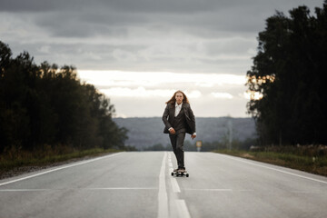 Man in grey office suit with long blond hairs is riding skateboard longboard down road outside the city on front view. Freedom from office work concept.