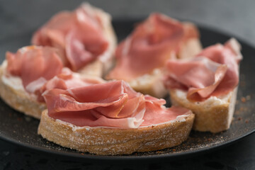 bruschetta with prosciutto and cream cheese on black plate closeup
