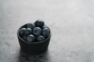 Fresh ripe blueberries in small black bowl on concrete background with copy space