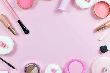 Flat lay with various makeup beauty products like brushes, powder or lipstick surrounding pastel pink background with blank copy space