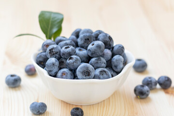 Fresh organic blueberries in white bowl on natural wooden background.