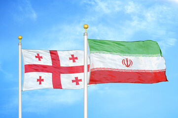 Georgia and Iran two flags on flagpoles and blue sky