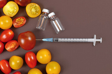 Concept for genetically modified food with tomatoes, injected syringe and empty medical vials on...