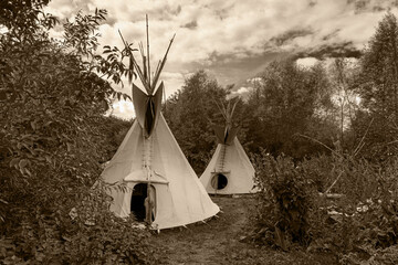 Two Indian tipis stand in a meadow in sepia and oil paint effect