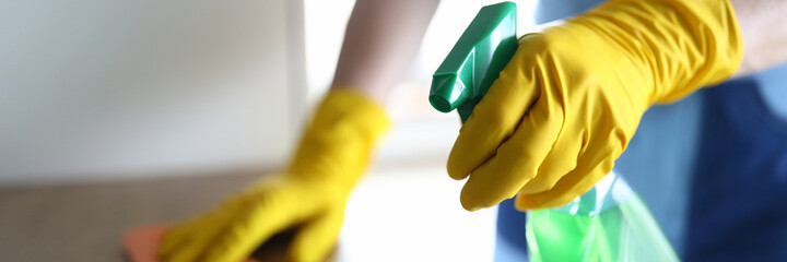Hands in yellow gloves disinfect with wooden table. Sanitize house without harm to health. Fight...